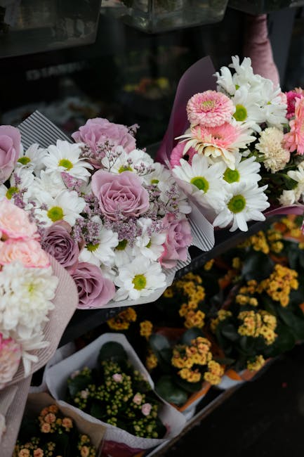 A selection of fresh floral bouquets arranged with pink and white flowers, including pale pink roses, white daisies with yellow centers, and white lilies, wrapped in light pink and purple wrapping pap